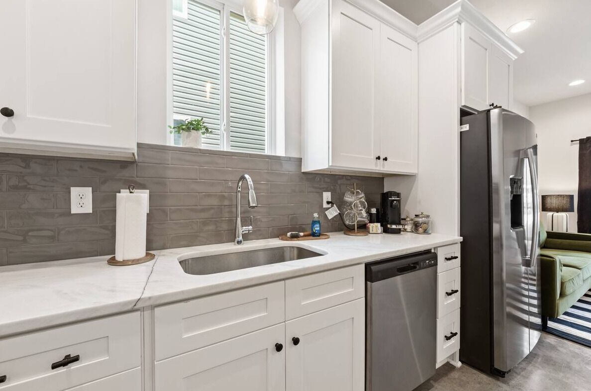 A modern kitchen with white cabinetry, a stainless steel refrigerator, and a built-in dishwasher.