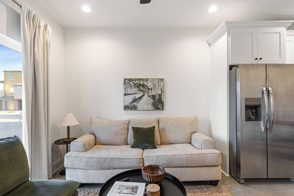 A modern living room with a sofa, a coffee table, a lamp, a painting, and a refrigerator.