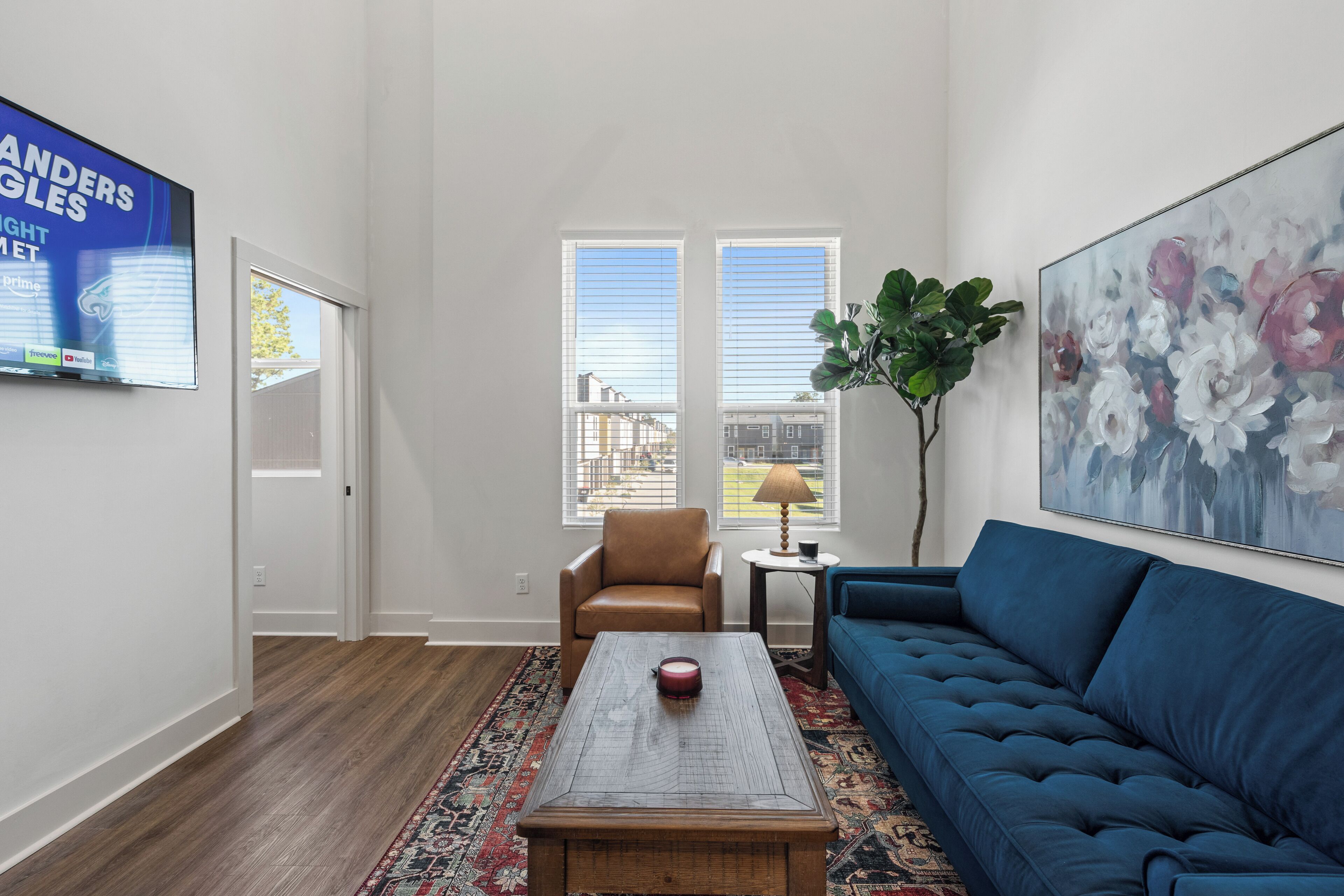 A living room with a wooden coffee table, a blue sofa, a brown armchair, and a large floral painting.