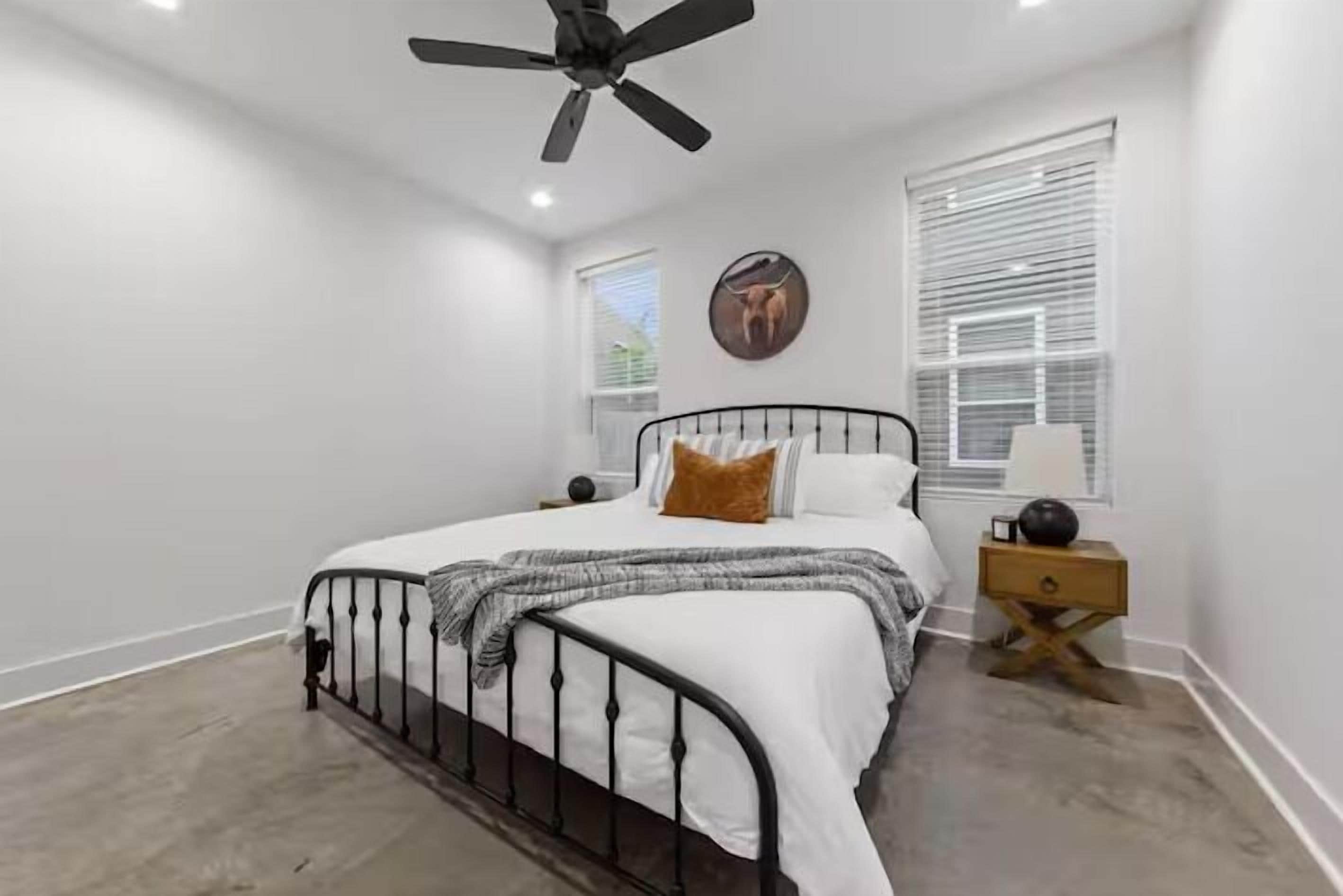 Une chambre à coucher avec un lit, un ventilateur de plafond, une fenêtre avec des stores et une horloge murale.