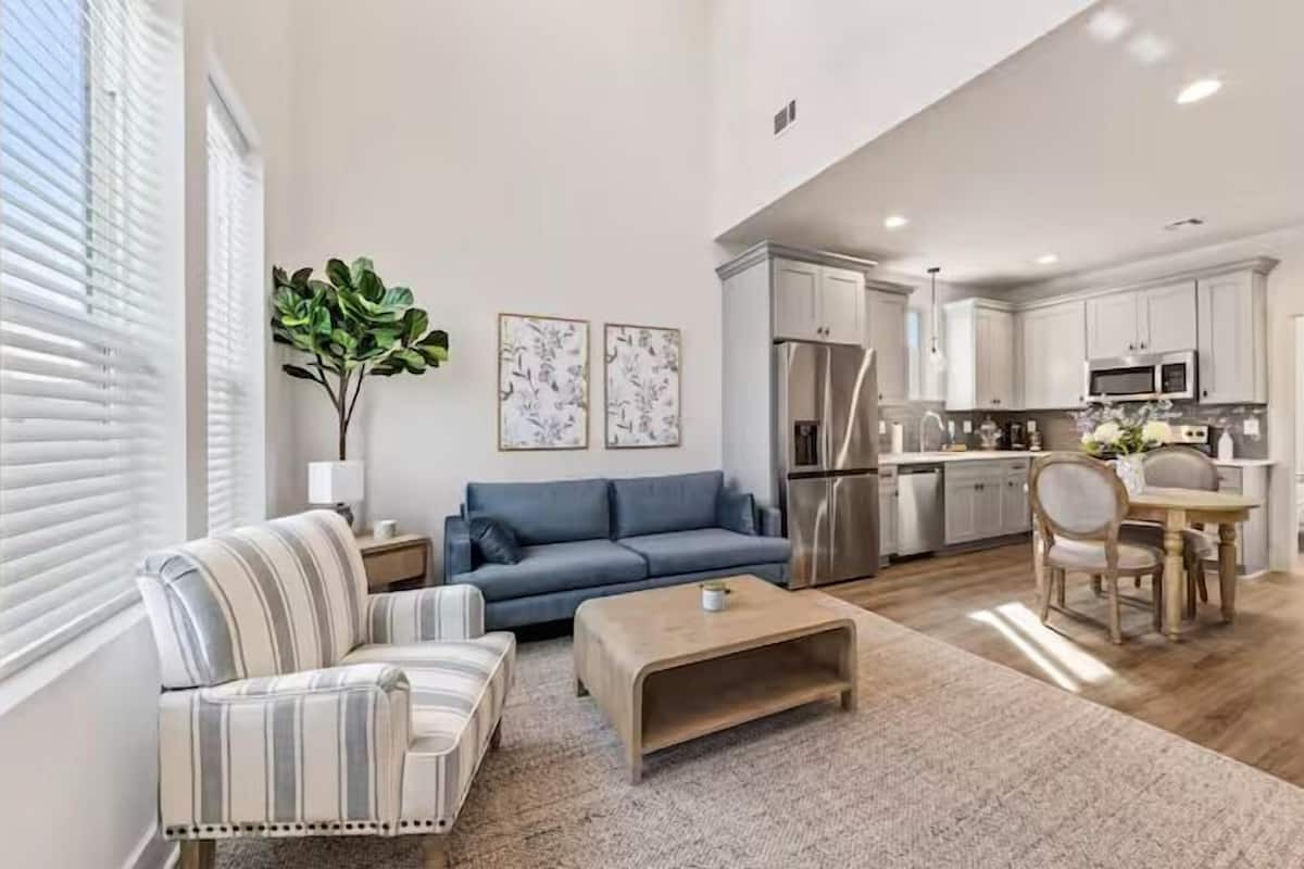 A modern living room with a sofa, armchair, coffee table, and a dining area with a table and chairs.