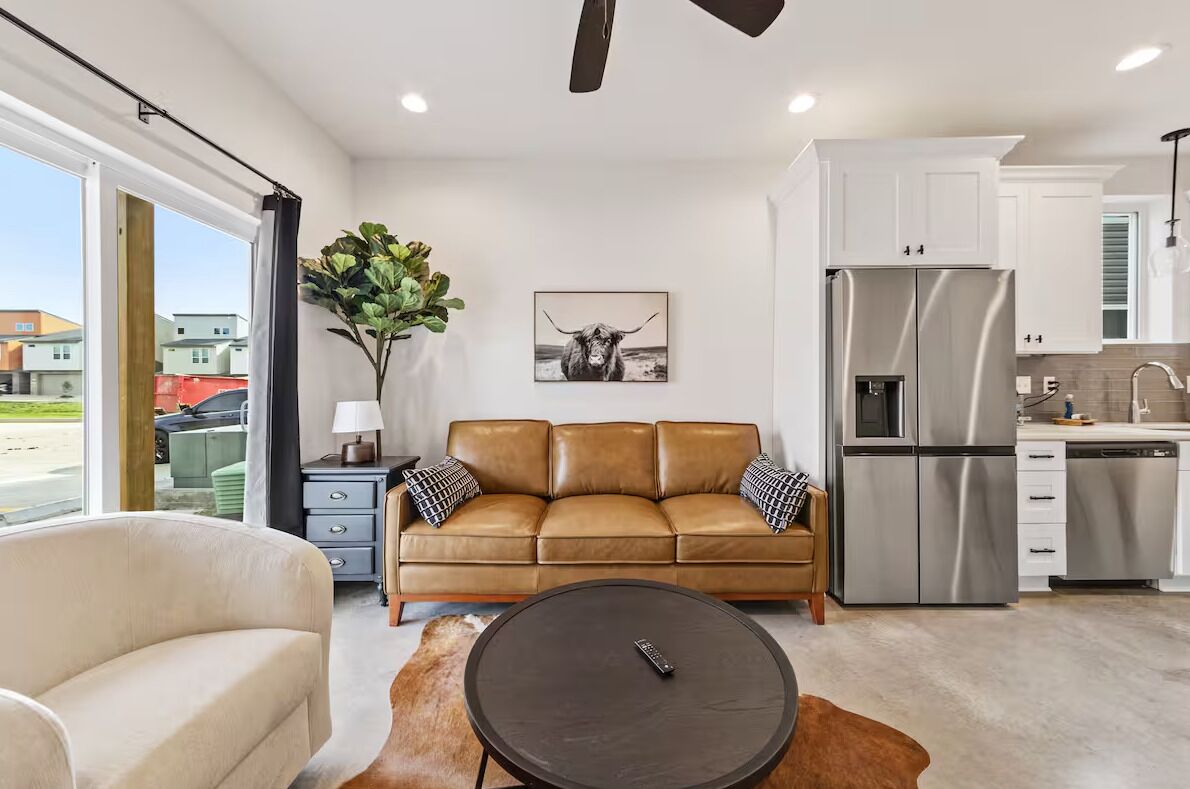 A modern living room with a leather sofa, a round coffee table, and a dining area with a white table and chairs.