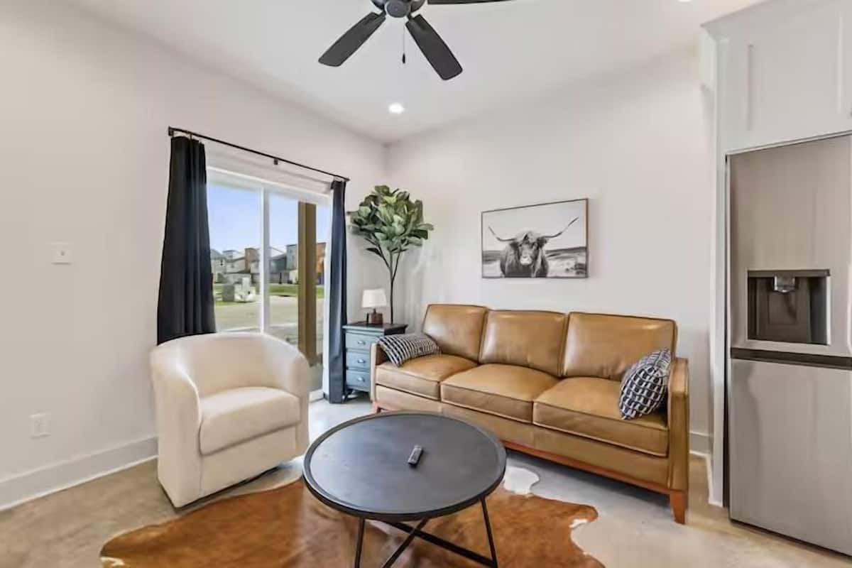 A living room with a sofa, a coffee table, a ceiling fan, a plant, and a refrigerator.