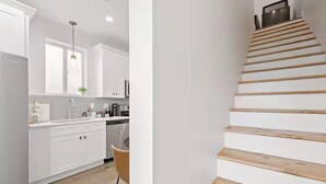Eine moderne Küche mit weißen Schränken, einer Holztreppe und Blick auf den Wohnbereich.
