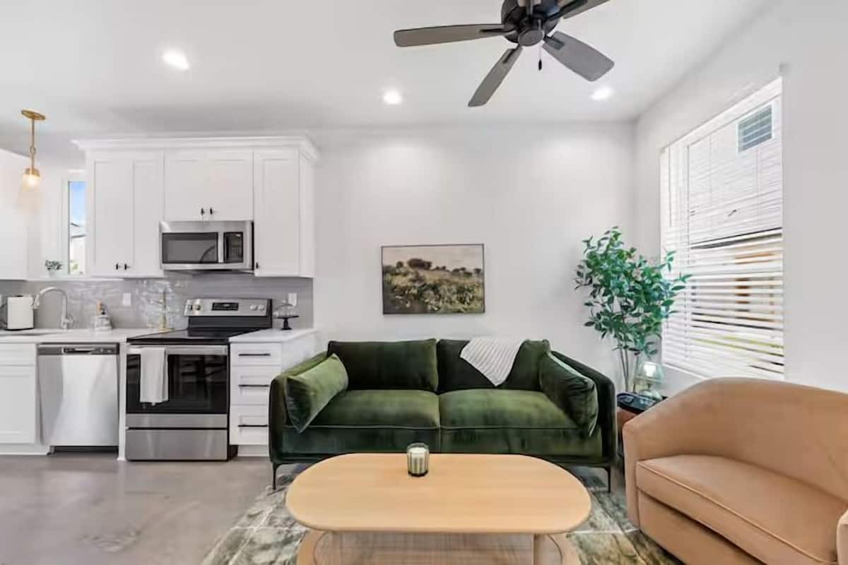 A modern kitchen with white cabinets, a microwave, and a stove. There is a green sofa and a beige couch in the living area.