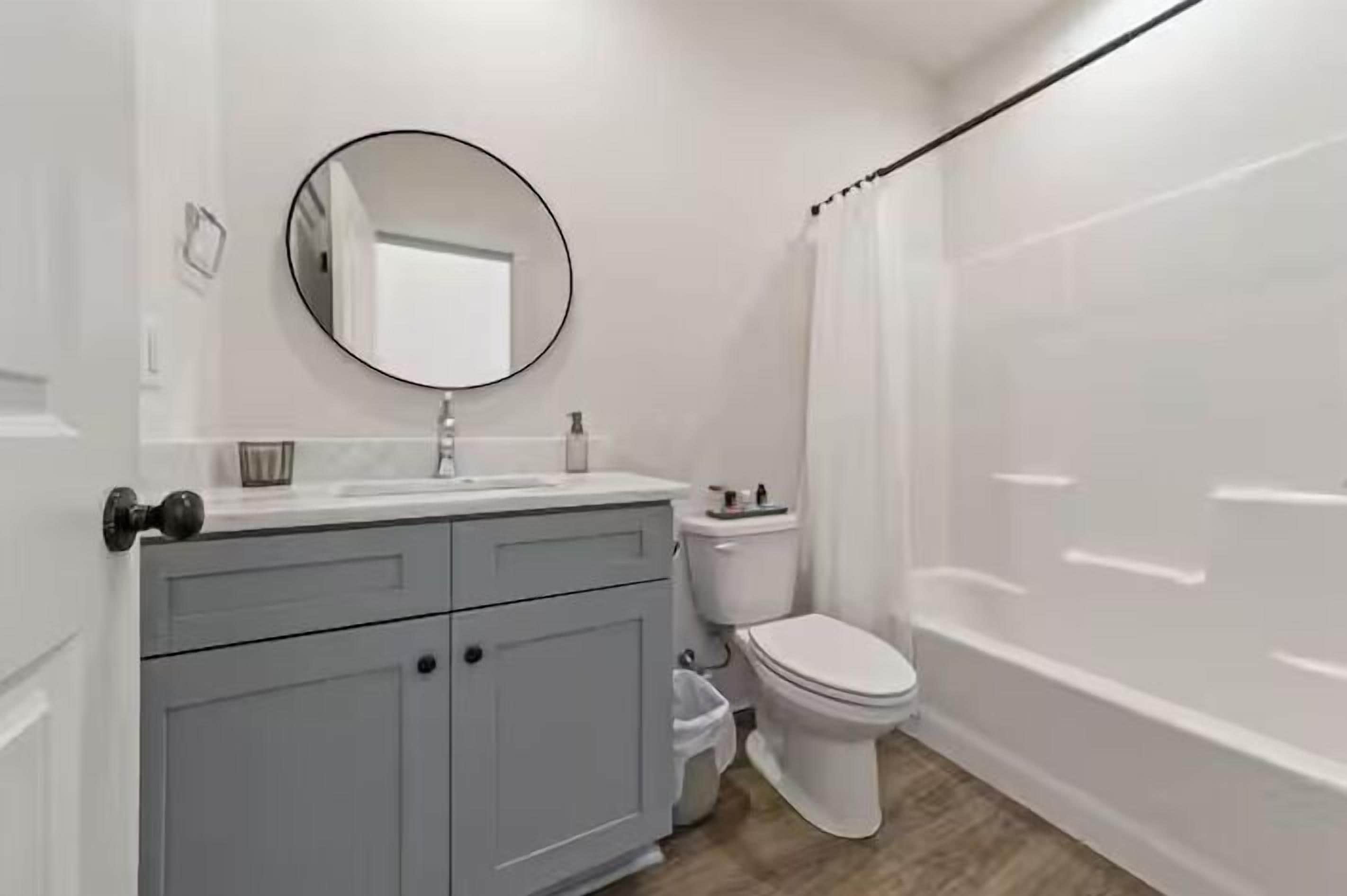 A bathroom with a white vanity, a round mirror, a toilet, and a shower curtain.