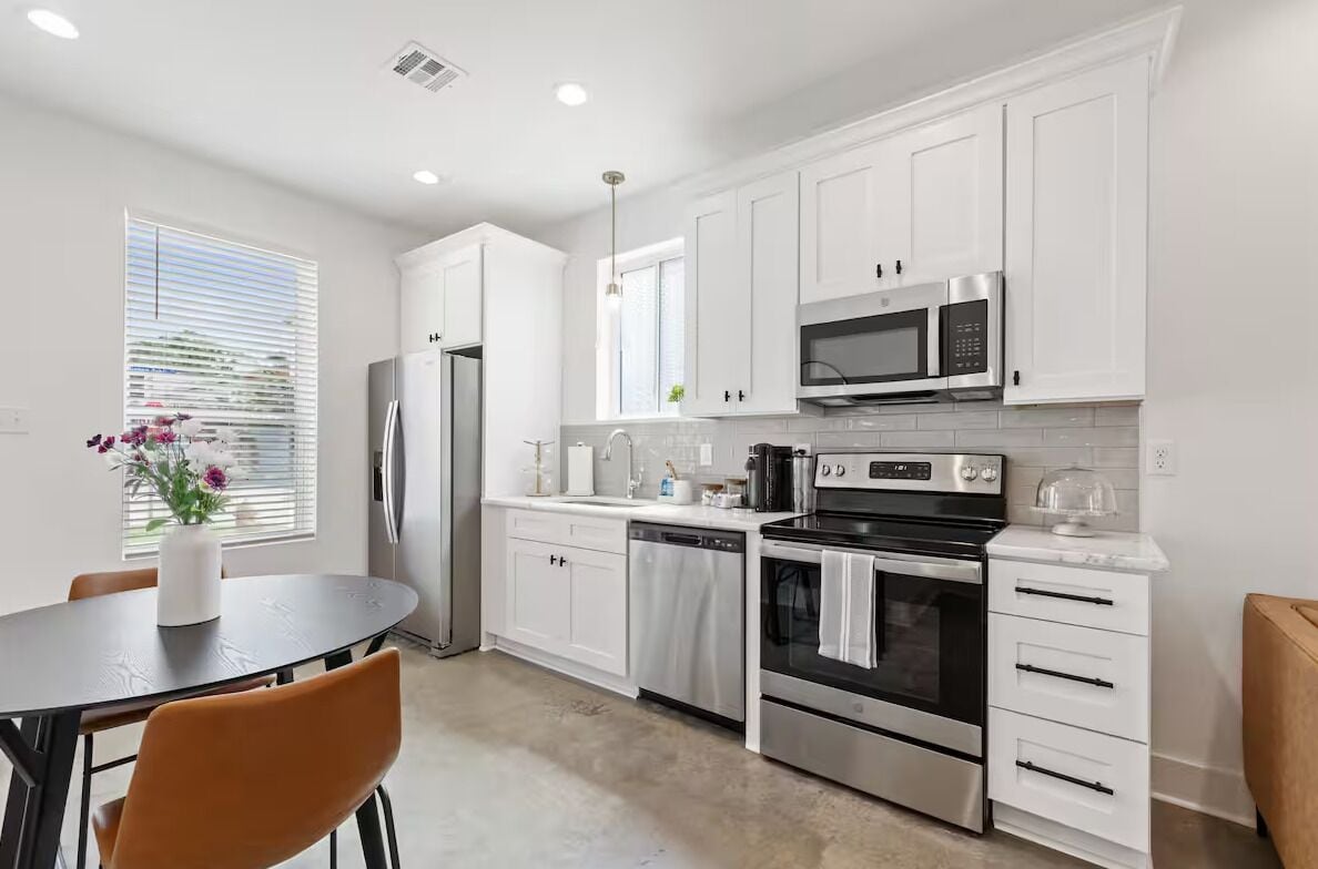 A modern kitchen with white cabinets, stainless steel appliances, and a dining area with a table and chairs.