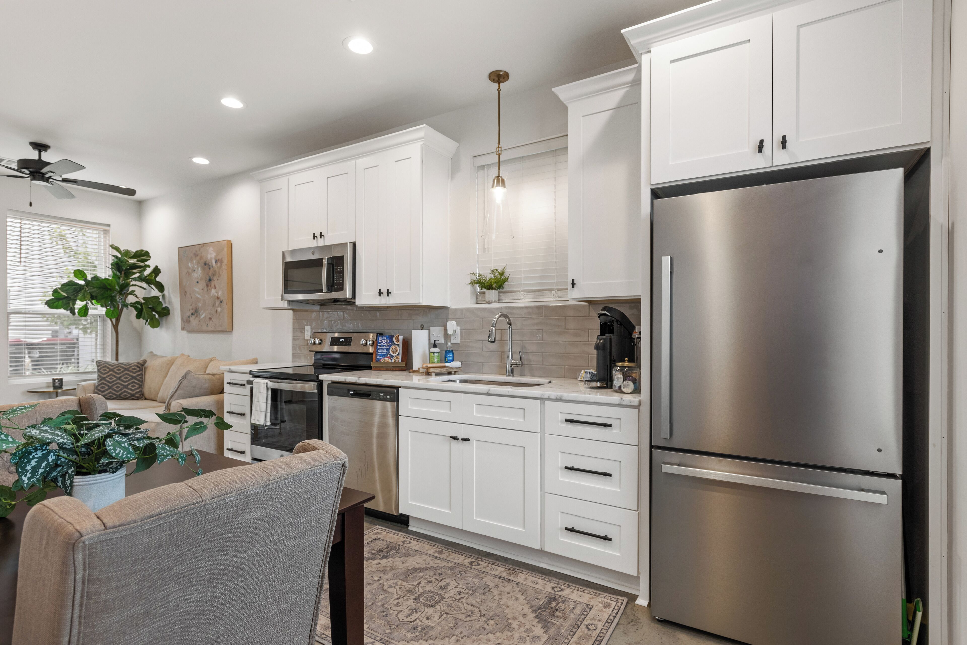 A modern kitchen with white cabinets, stainless steel appliances, and a dining area with a sofa and coffee table.