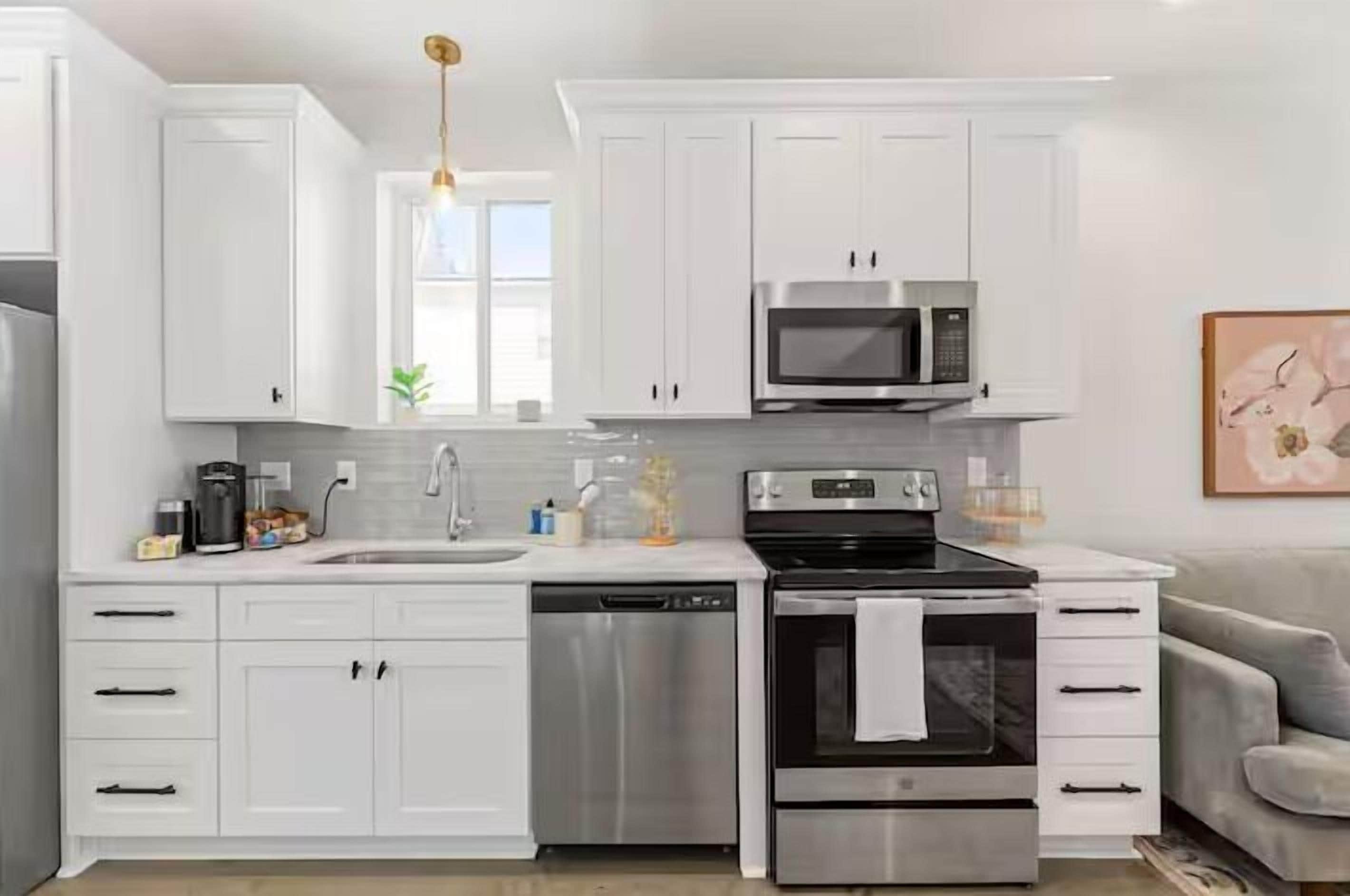 A modern kitchen with white cabinets, a stainless steel dishwasher, an oven, and a microwave.