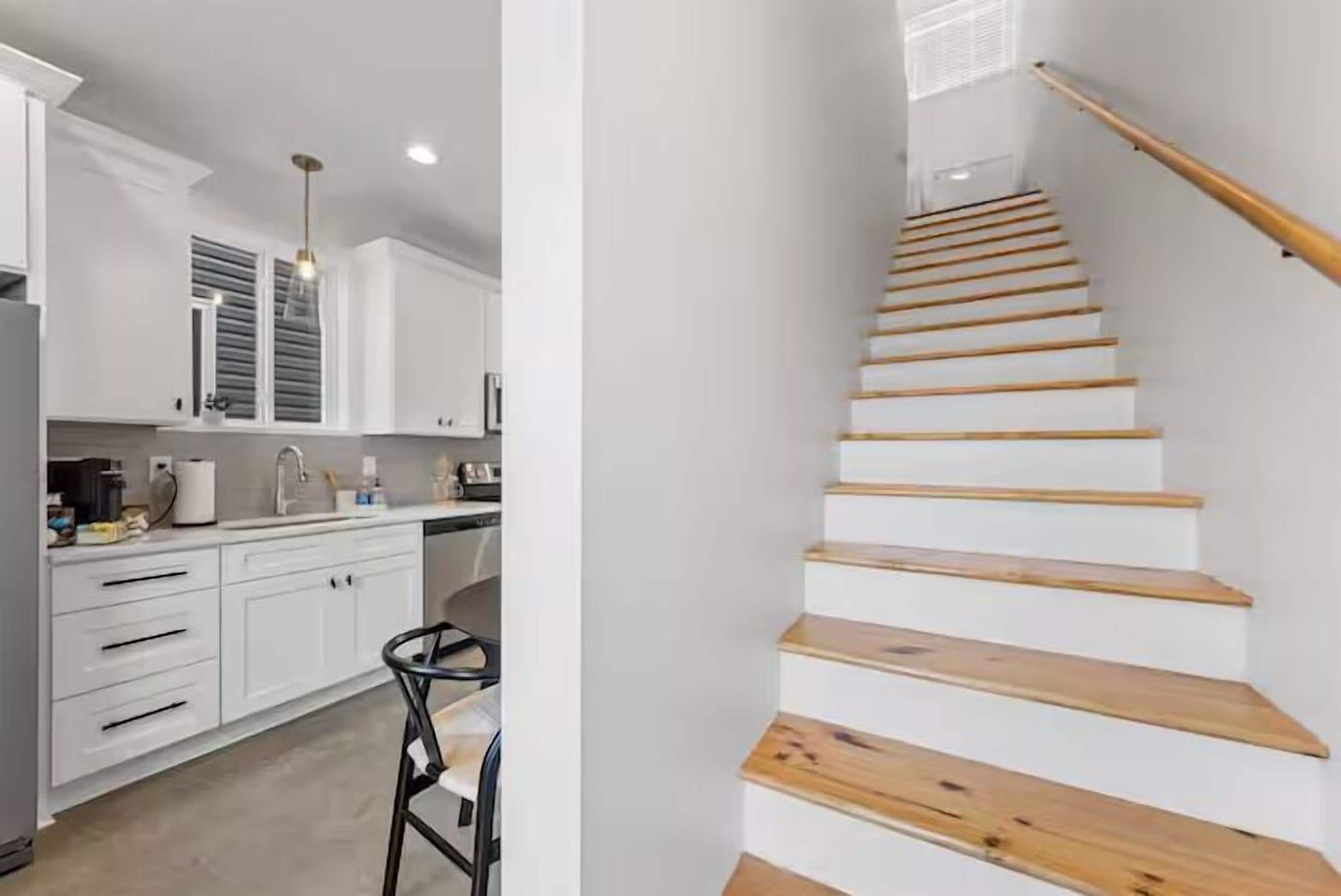 A modern kitchen with white cabinets and a wooden staircase.