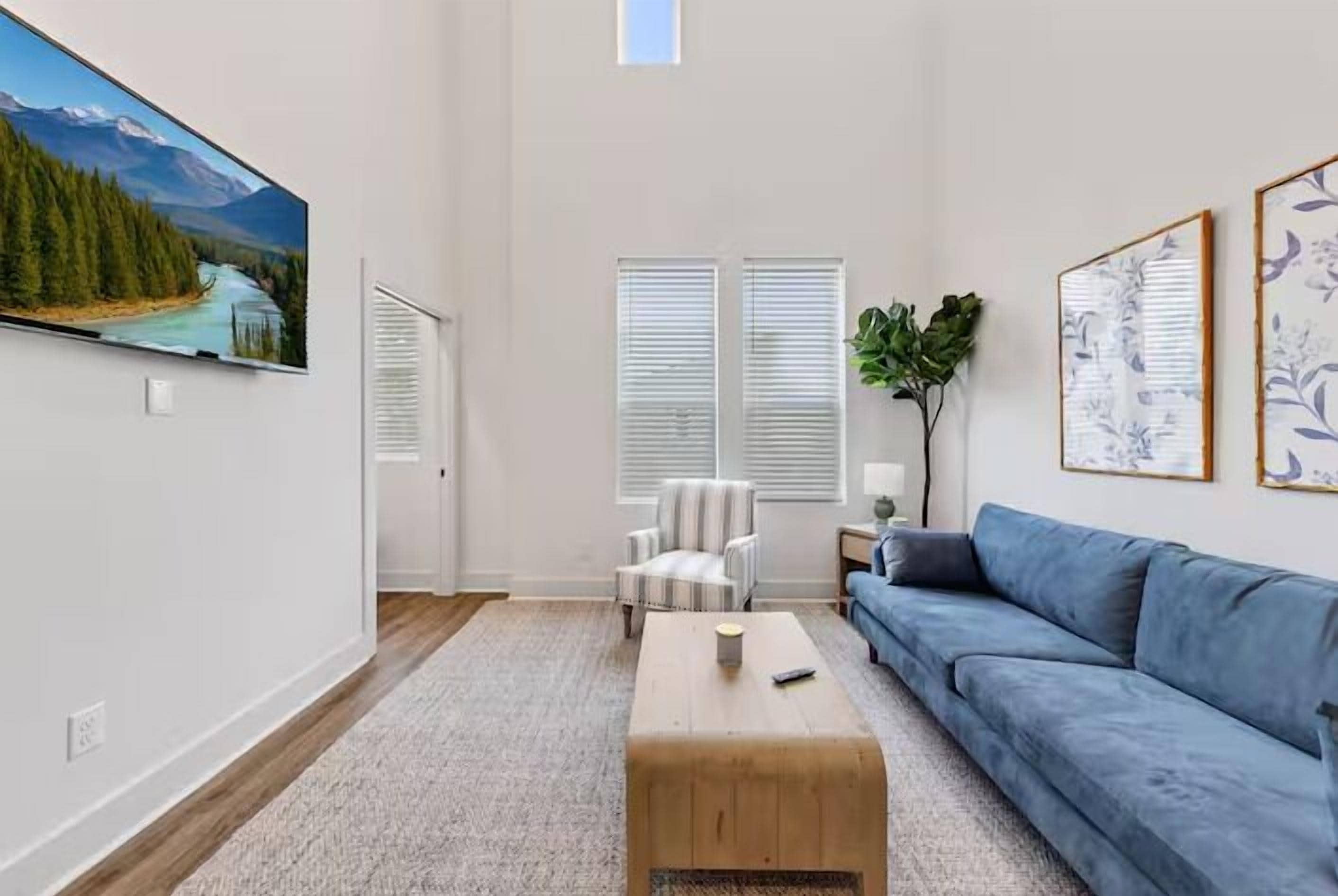 Una sala de estar con un televisor de pantalla plana grande, un sofá azul, una mesa de centro de madera y un sillón a rayas.