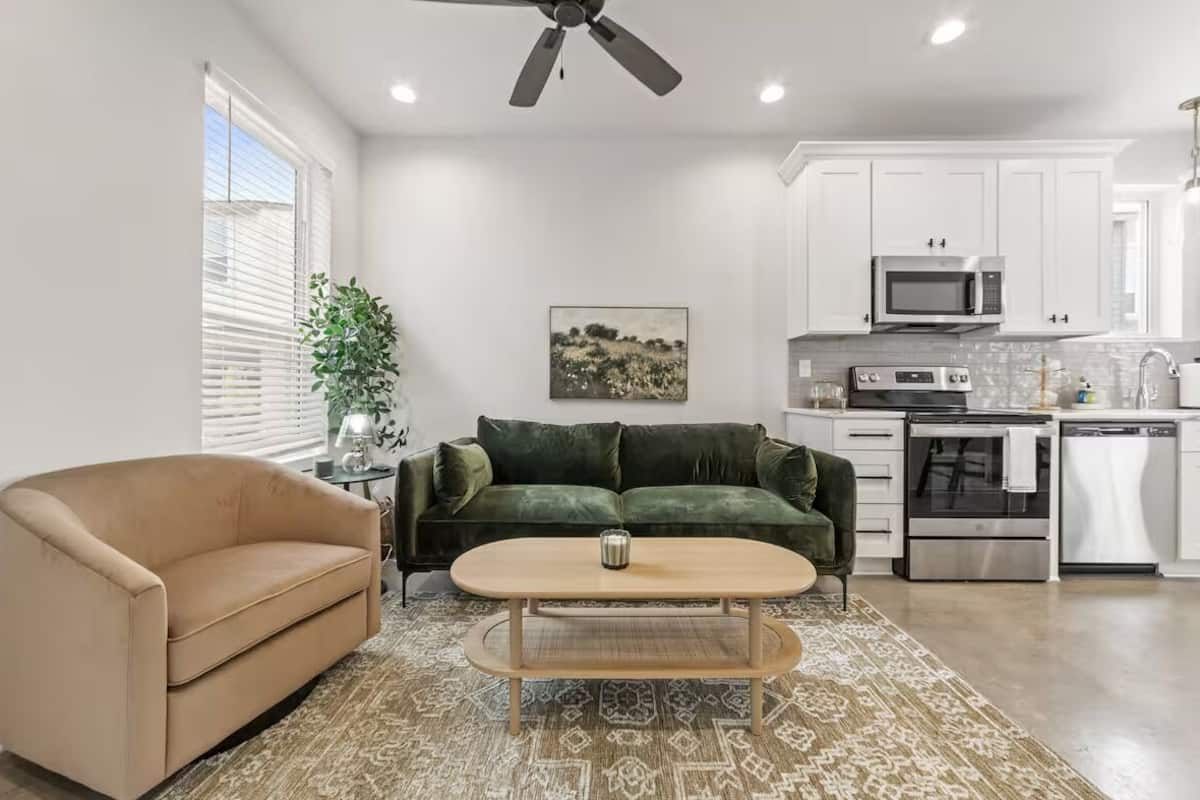 A modern living room with a beige sofa, a green velvet couch, and a wooden coffee table.