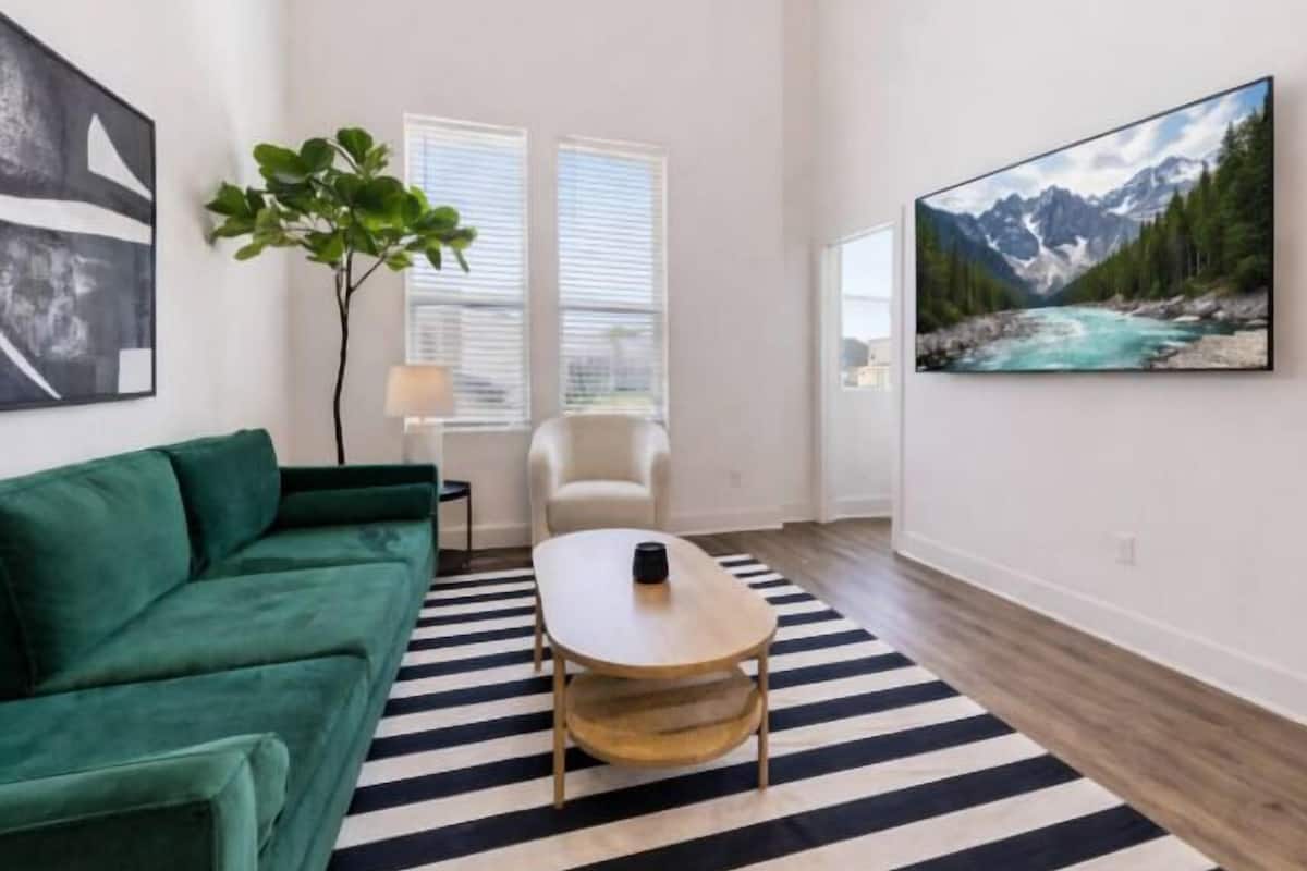 A modern living room with a green sofa, a round coffee table, and a black and white striped rug.