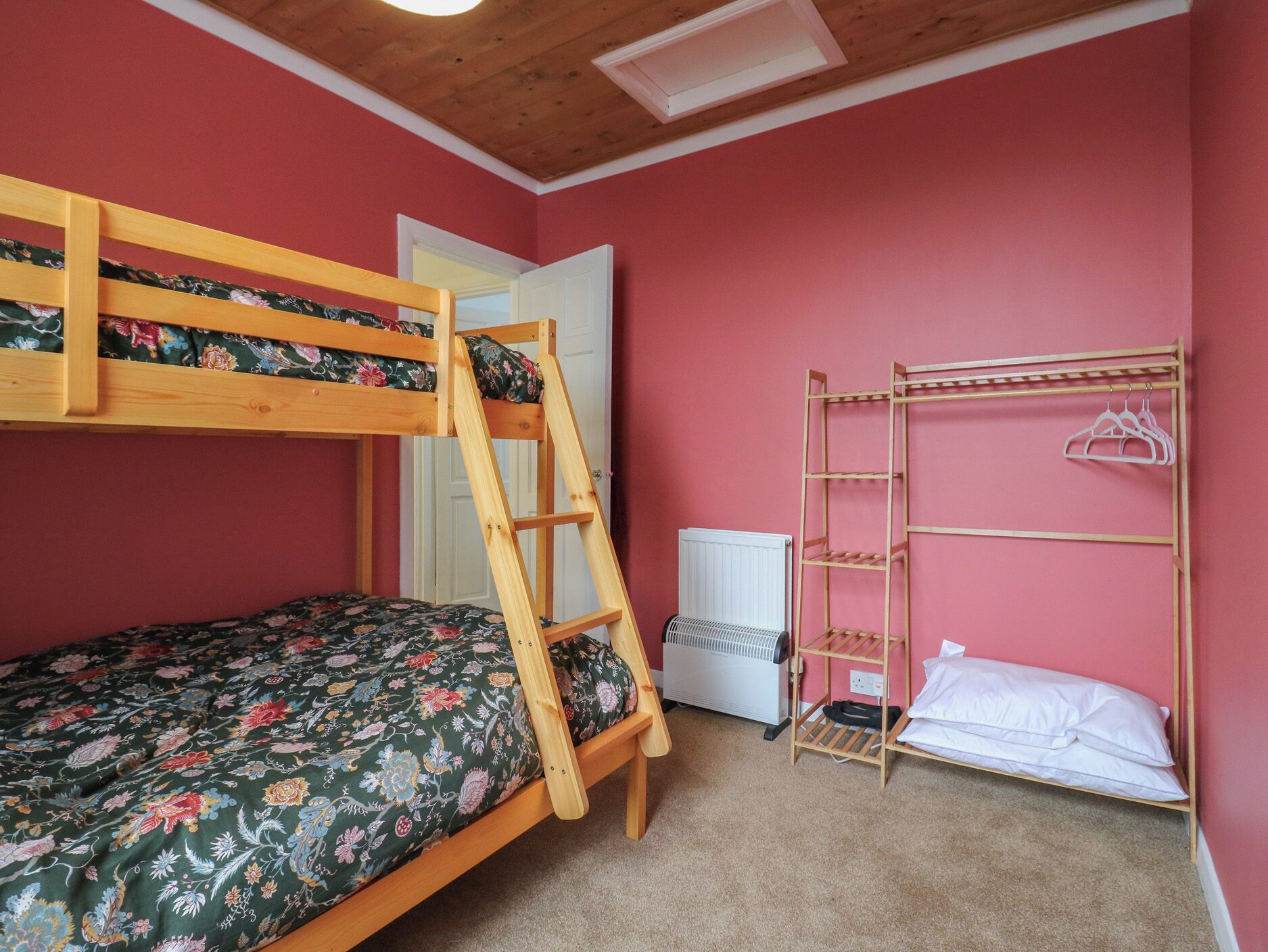 A bunk bed with a wooden ladder, a small white radiator, and a wooden shelf unit with hangers.