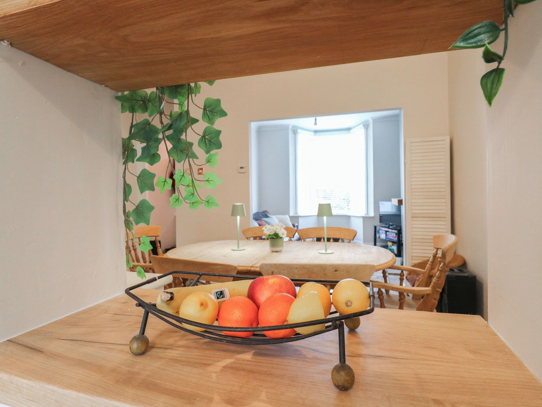 Comedor con una mesa redonda, sillas, una cesta de frutas y vistas a una ventana y una puerta.