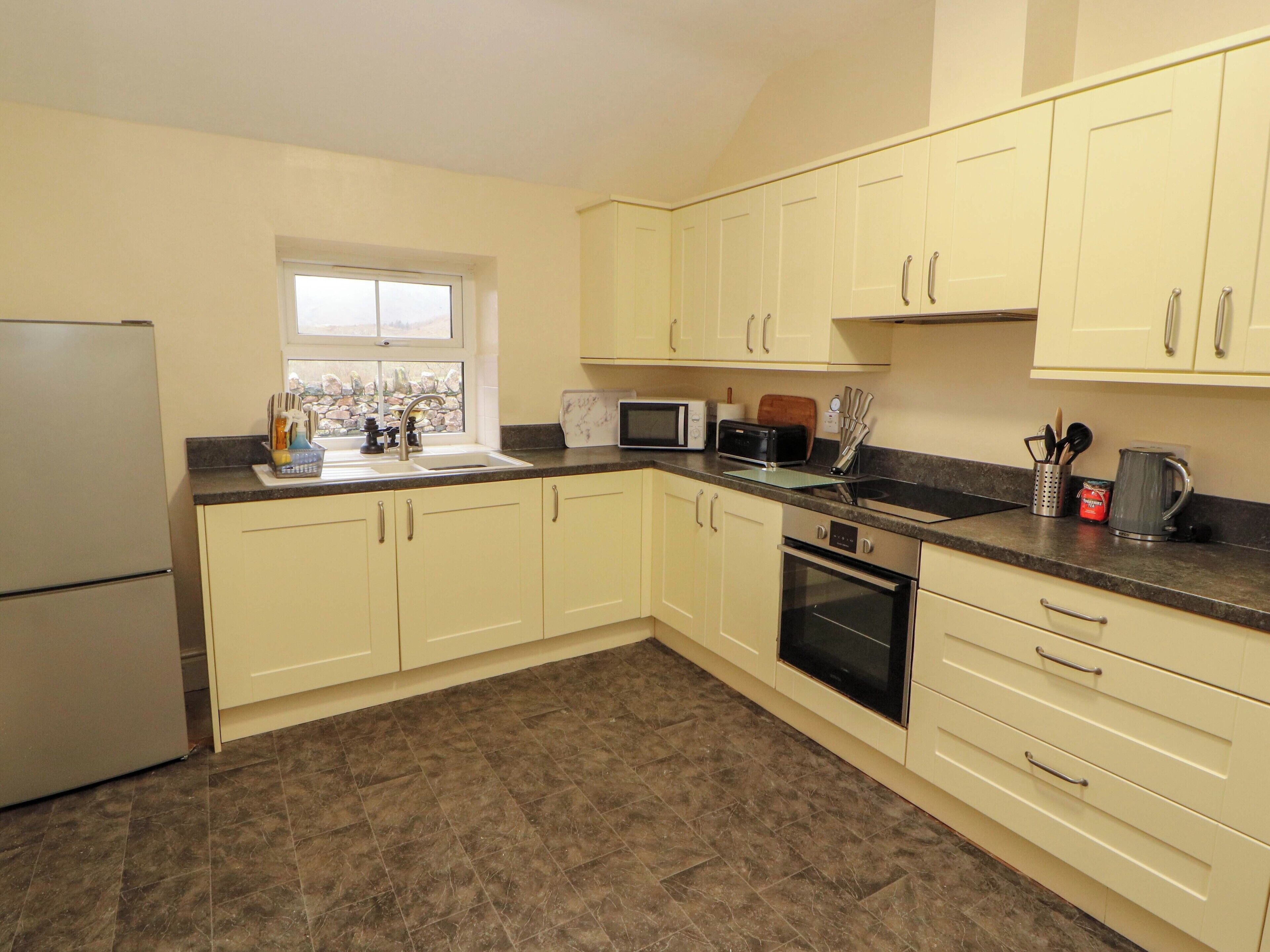 A kitchen with cream-colored cabinets, a refrigerator, a microwave, a toaster, and a sink.