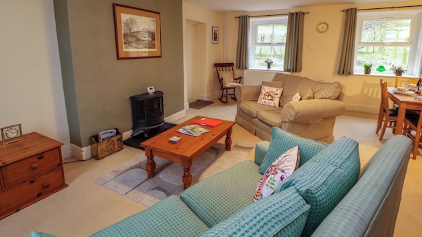 A cozy living room with a sofa, a wooden coffee table, a fireplace, and a dining area with a table and chairs. - Easthwaite Cottage (Seascale)