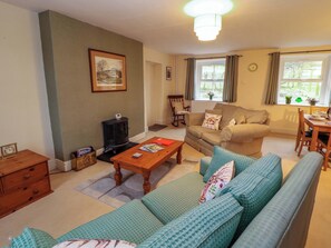A cozy living room with a sofa, a wooden coffee table, a fireplace, and a dining area with a table and chairs. - Easthwaite Cottage (Seascale)