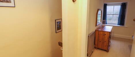 A hallway with a wooden dresser, a radiator, and a window with curtains.
