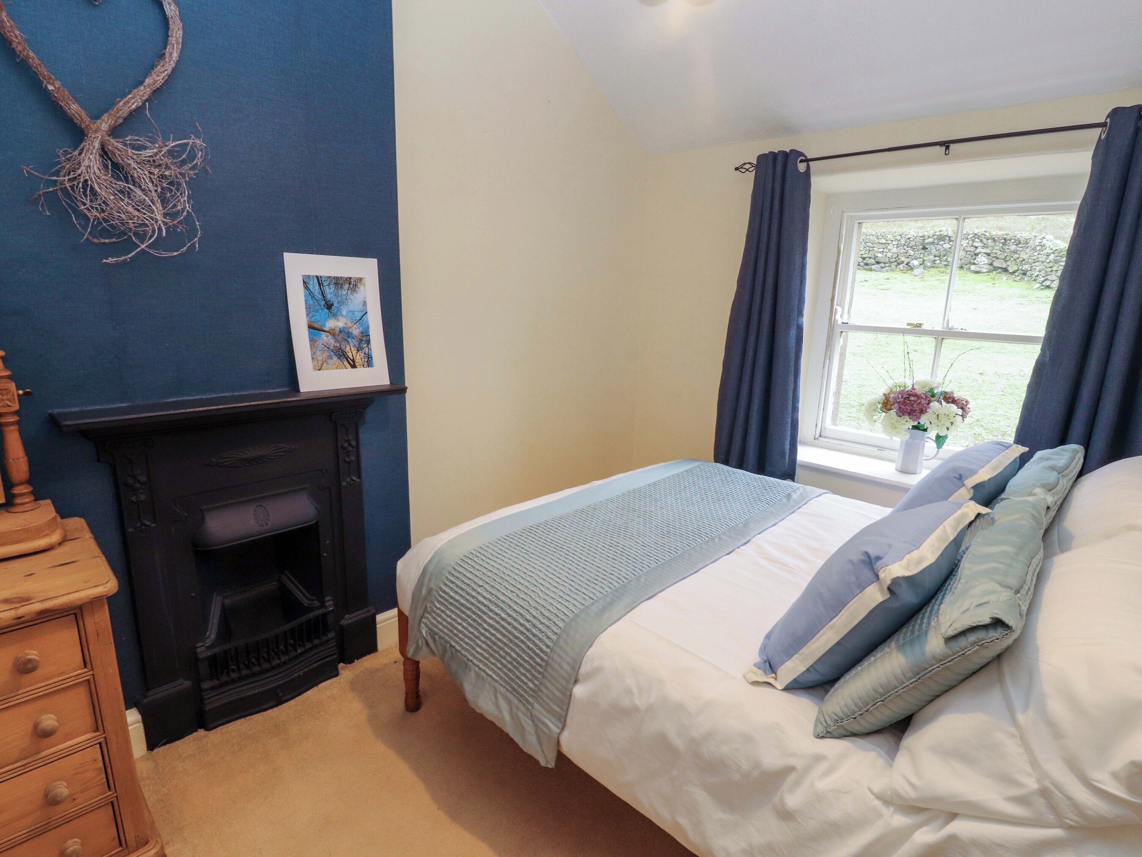 A bedroom with a bed, a fireplace, a dresser, and a window with curtains.