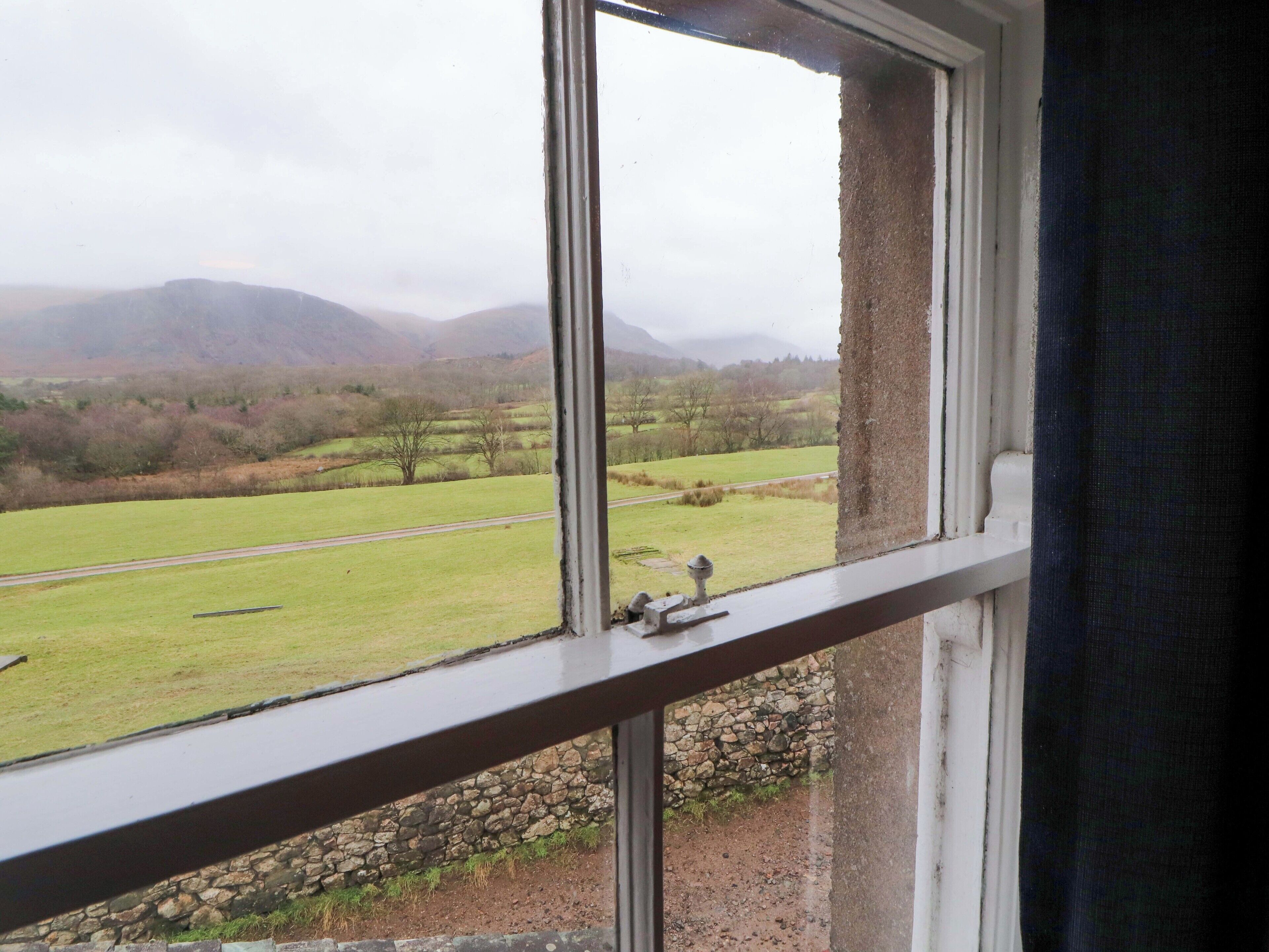 A view from a window overlooking a rural landscape with a stone wall and a road.