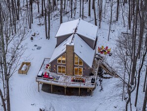 A cabin with a large deck, a chimney, and a snow-covered roof. - A-Frame Escape ~ Hot Tub, Sauna, Game Room, Gym (Big Bass Lake)