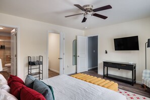 A bedroom with a bed, a ceiling fan, a TV mounted on the wall, a bedside table, and a door leading to another room. - A-Frame Escape ~ Hot Tub, Sauna, Game Room, Gym (Big Bass Lake)