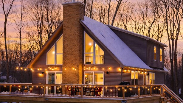 A two-story house with a large chimney, multiple windows, and a deck with string lights.