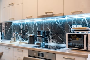 A modern kitchen with a black marble backsplash, a coffee maker, a microwave, and a built-in oven. - Filarmonikis Deluxe Apartment (Kerkira)