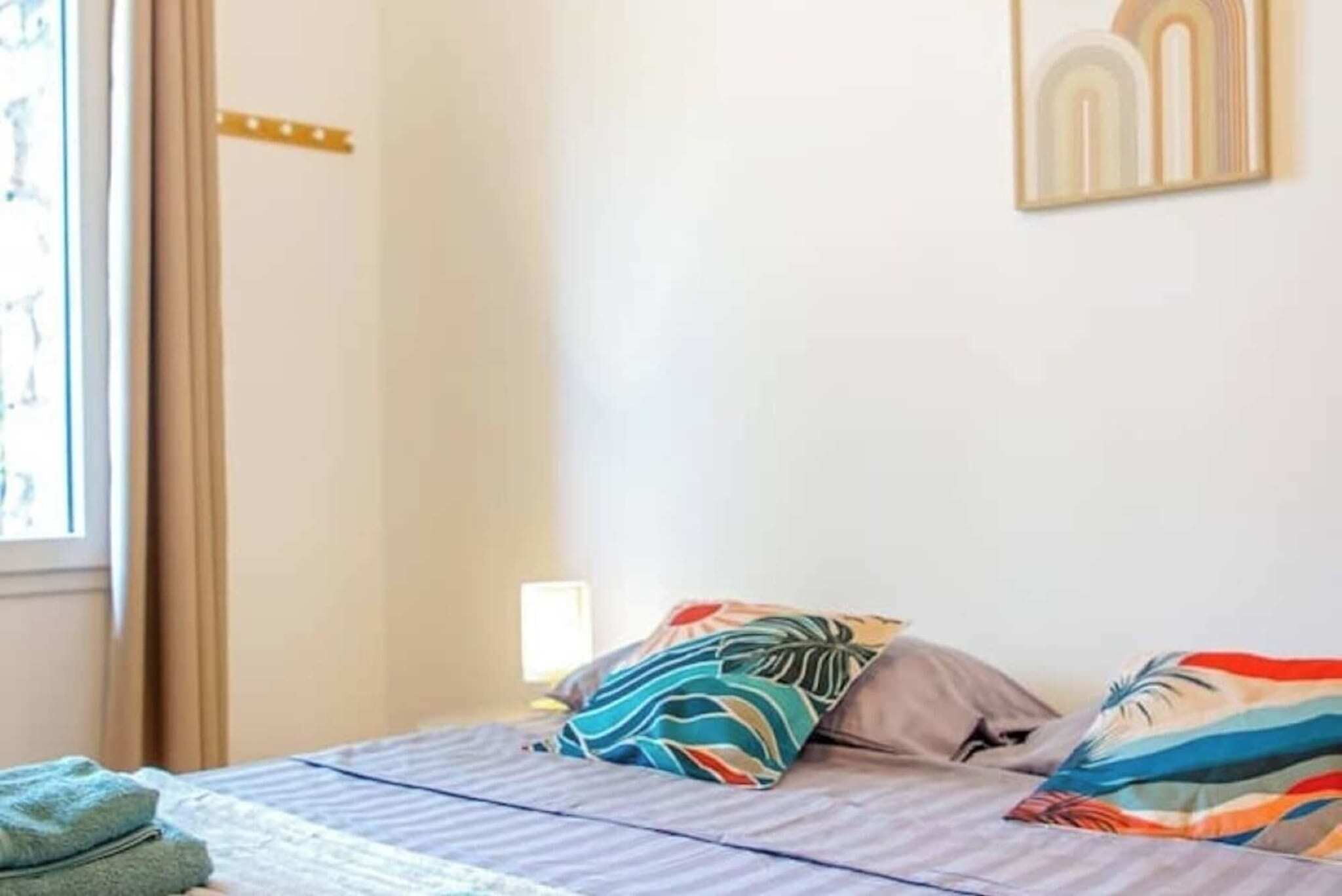 Une chambre à coucher avec un lit, des oreillers, une fenêtre et une œuvre d’art accrochée au mur.