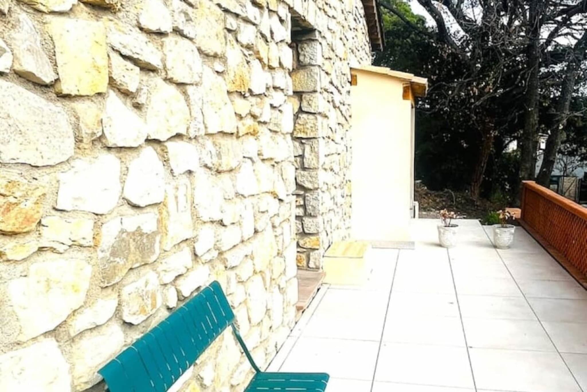 Un mur de pierre, un banc, un petit bâtiment et une terrasse carrelée.