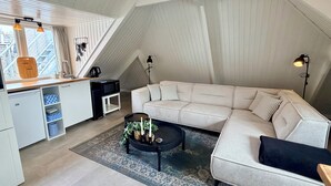 Un espai tipus loft amb un sofà blanc, una taula de centre, una cuina amb microones i una finestra amb cortines.