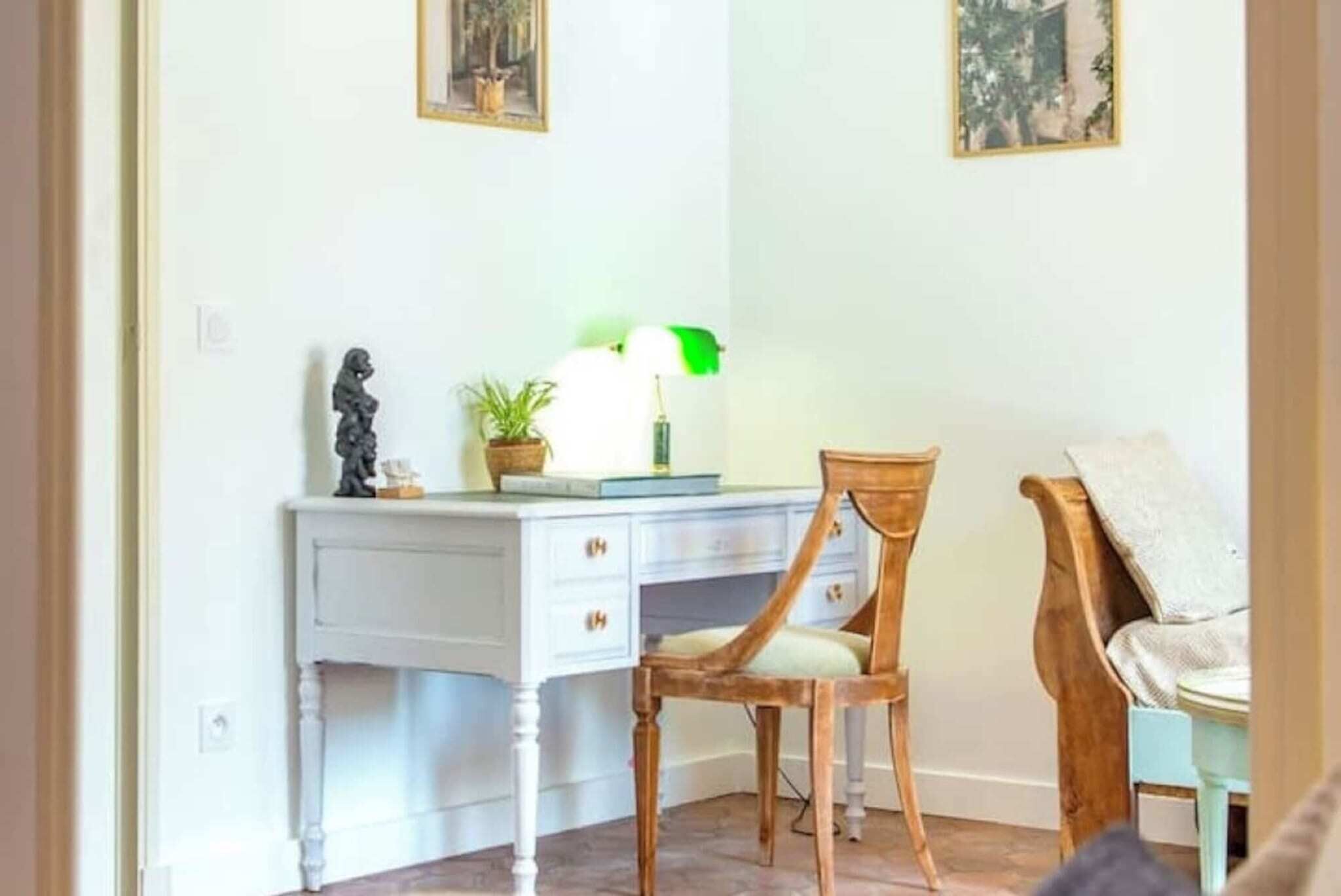 Une pièce avec un bureau blanc, une chaise en bois, une lampe et une petite plante.