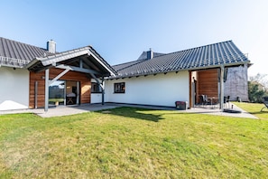 Une maison moderne dotée d’un patio couvert, d’une terrasse en bois et d’une pelouse.