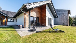 Ett modernt hus med en täckt uteplats, en gräsmatta och en klar himmel.