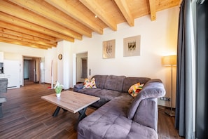 Un salon moderne avec un plafond en bois, un canapé d’angle, une table basse et un lampadaire.