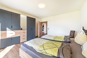 Une chambre moderne dotée d’une grande armoire, de deux lits avec une literie à motifs et d’un petit coin salon.