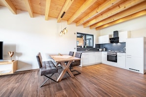 Une cuisine moderne avec des meubles blancs, une table à manger en bois et un four encastré.
