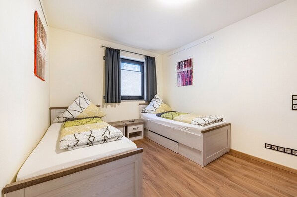 A bedroom with two beds, a window with curtains, a bedside table, and a wall-mounted artwork. - Apartment “Staufenberg Chalets” with Wi-Fi (Berschweiler)