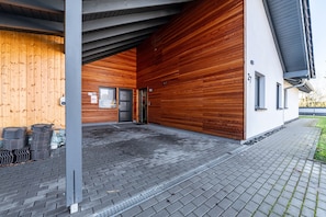 Ein modernes Gebäude mit Holzfassade, überdachter Eingang und einem gepflasterten Weg.