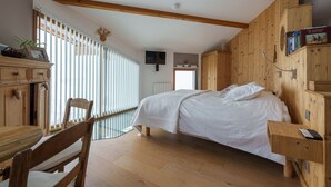Quarto com paredes de madeira, uma cama, uma escrivaninha e uma cadeira.