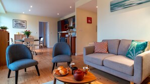 Una sala moderna con un sofá, dos sillones, una mesa de comedor con sillas y una cocina al fondo.