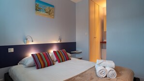 Una habitación de hotel con cama, un cuadro en la pared, una mesita de noche y la puerta del baño.