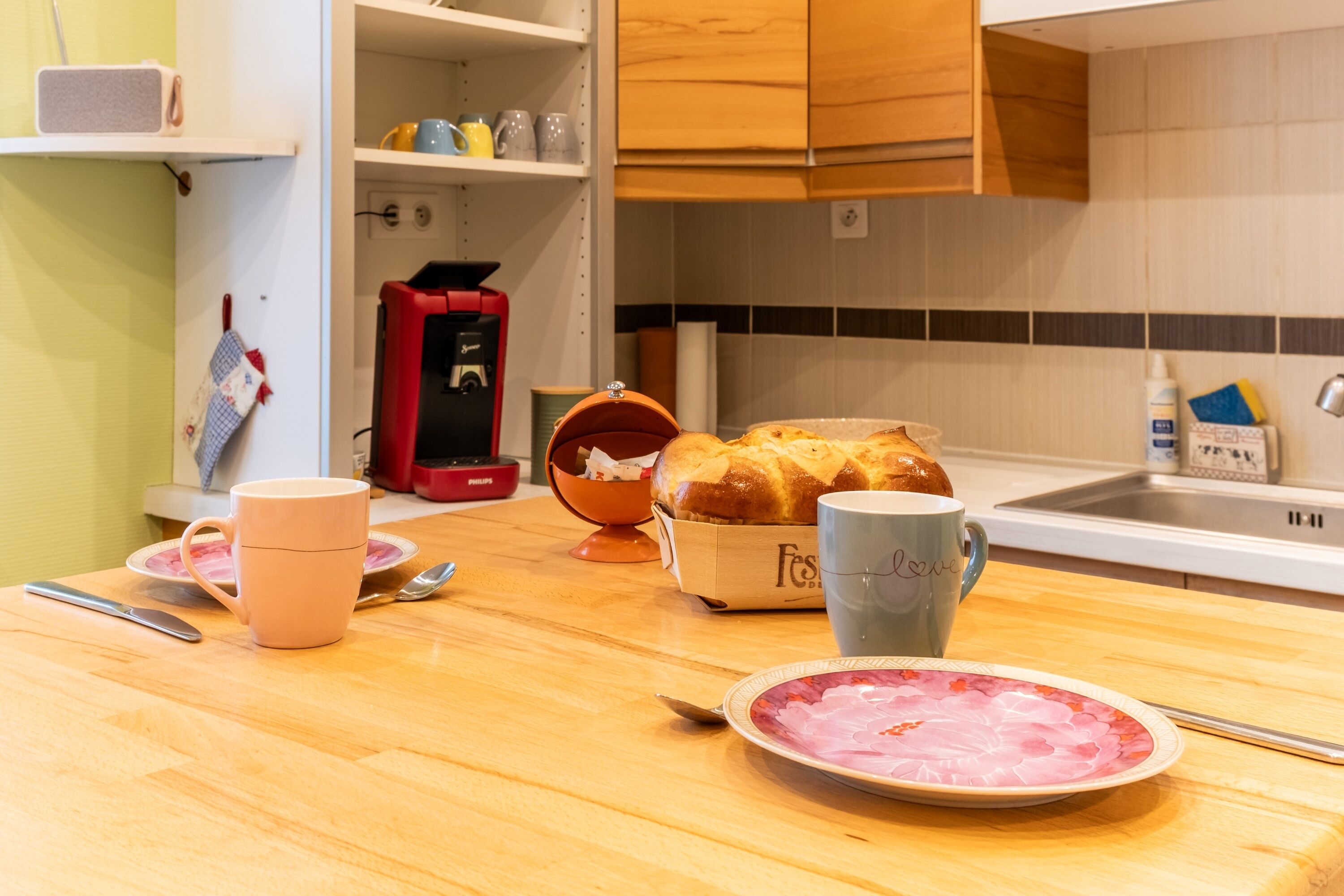 Eine Küche mit einer Holzausziehtischplatte, einer Kaffeemaschine, einer Brokasten, einer Tasse und einem Teller mit Essensresten.