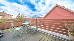 A wooden deck with green metal chairs and a small round table, a red wooden fence, and a clear blue sky. - Le Repos du Rhin - 20min de Mulhouse (Niffer)