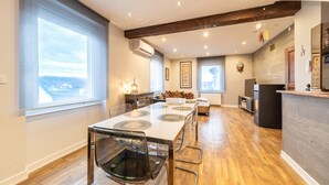 A spacious dining area with a long table and chairs, a kitchen area with a counter, and a large window providing a view. - Le Repos du Rhin - 20min de Mulhouse (Niffer)