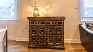 A wooden cabinet with intricate carvings and a lit lantern on top, placed in a room with wooden flooring and a window. - Le Repos du Rhin - 20min de Mulhouse (Niffer)