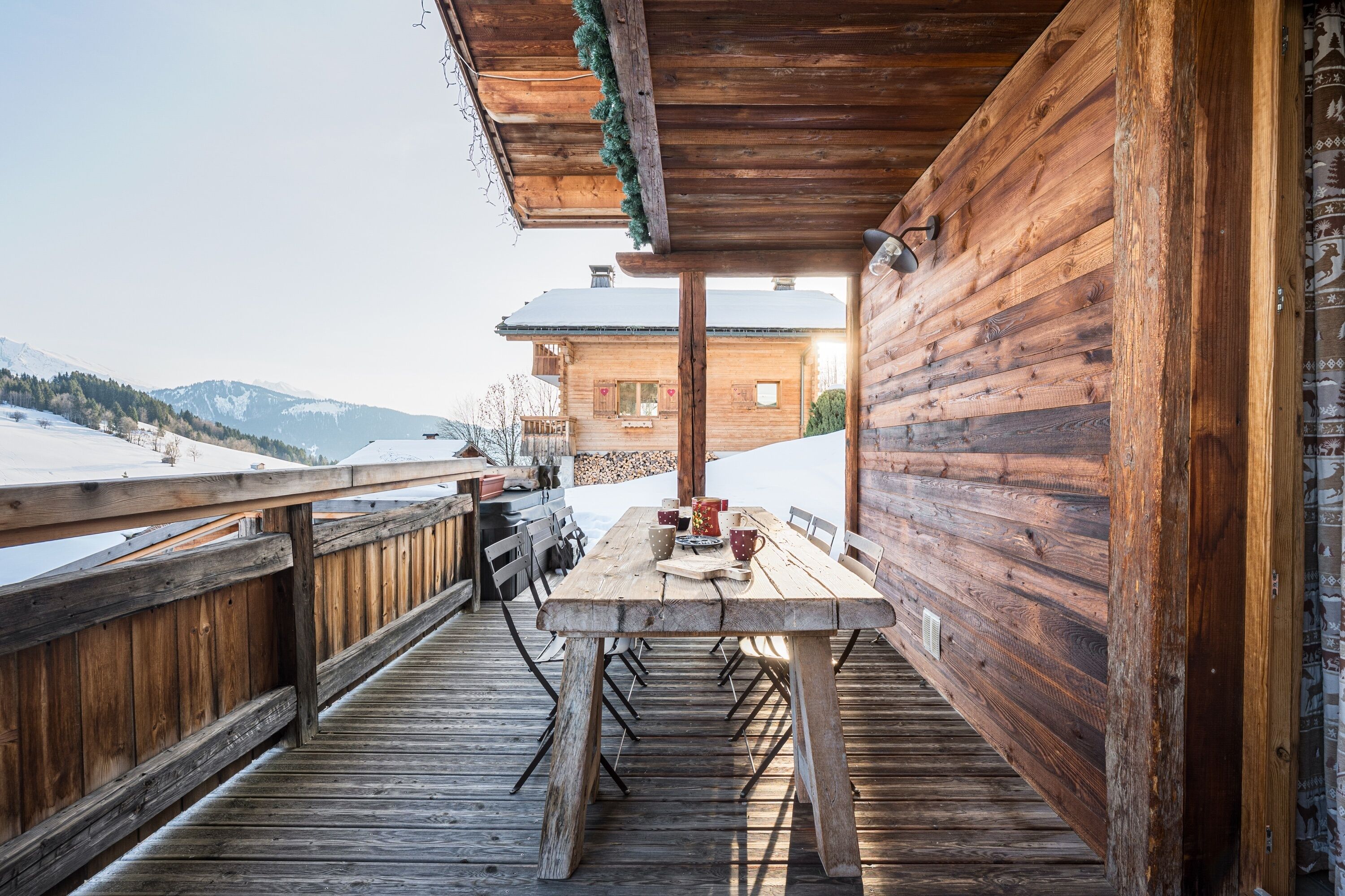 Una terraza de madera con una mesa y sillas, con vistas a un paisaje nevado y una montaña.