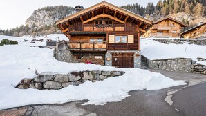 Eine Holzhütte mit Steinfundament, mehreren Balkonen und Blick auf einen verschneiten Berg.