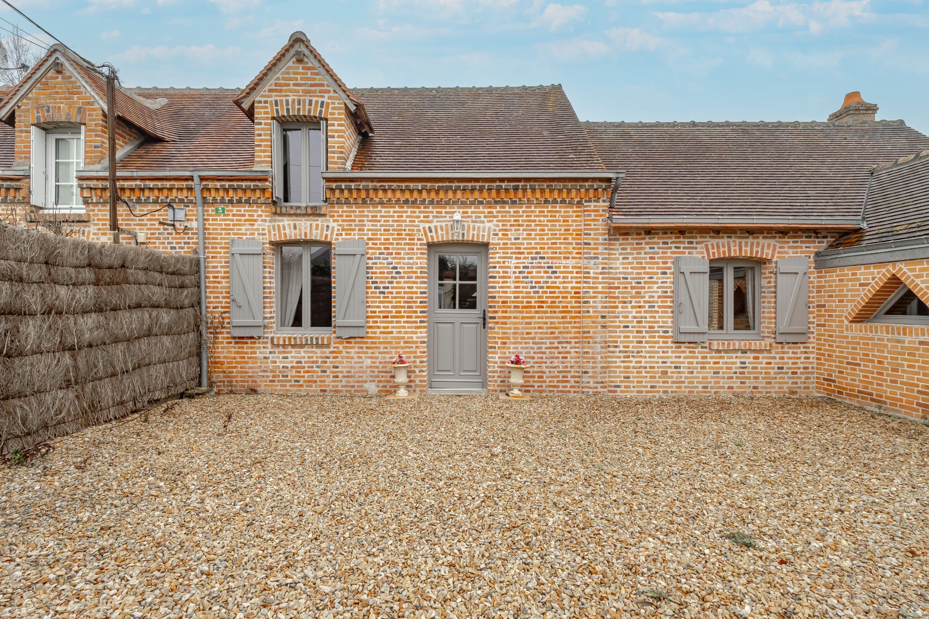 Une maison en briques avec une allée en gravier, une clôture en bois et un petit jardin.